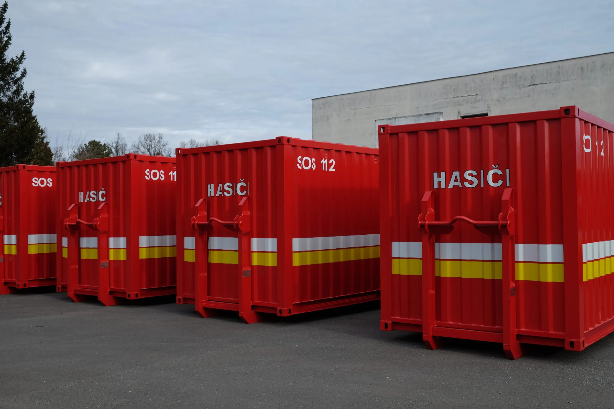 Reihe roter Hakenlift-ISO-Module in Feuerwehrlackierung mit Reflexstreifen, bereitgestellt auf einem Depothof