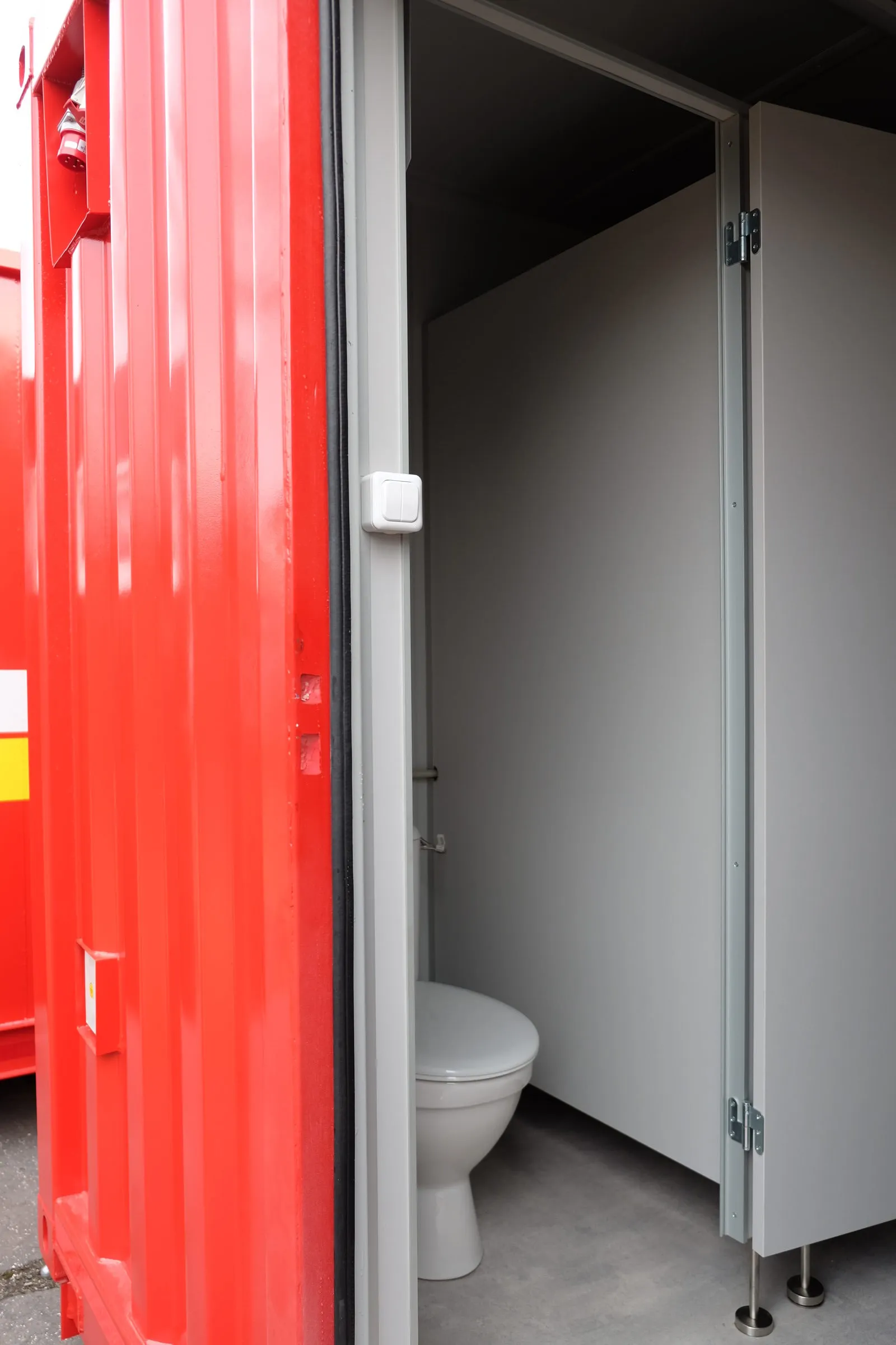 WC-hytt inne i en röd sanitetsmodul, sedd genom den öppna dörren